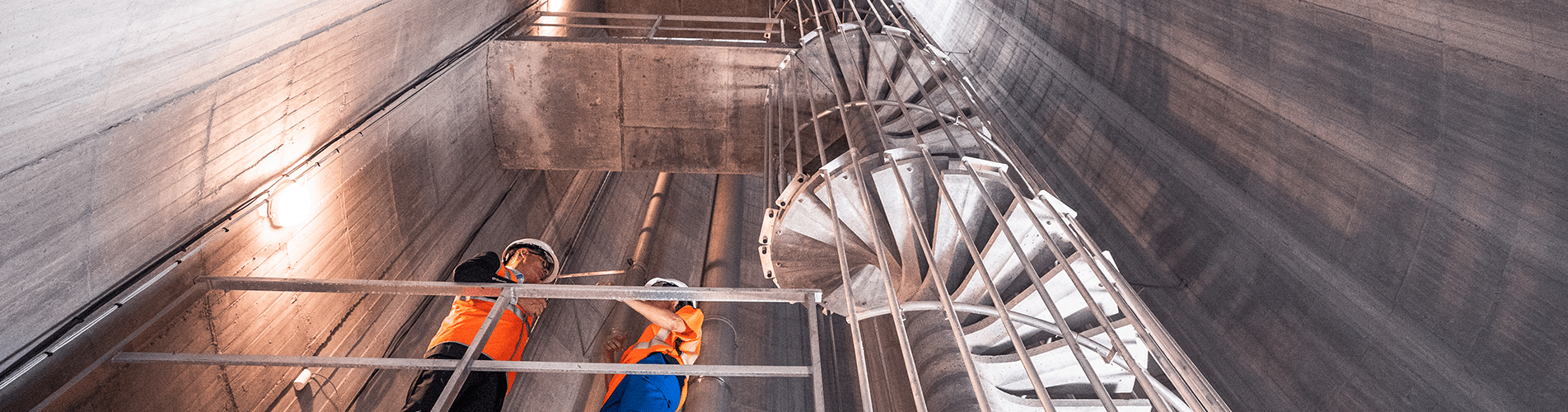 Photo décorative prise en contre-plongée. Elle montre l'escalier intérieur d'ascension jusqu'à la cuve du château d'eau. Deux salariés de la RESE échangent au niveau du premier pallier.