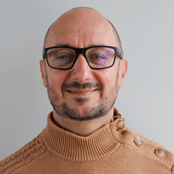 Photo d'identité d'un homme blanc au crâne rasé avec une légère barbe portant des lunettes